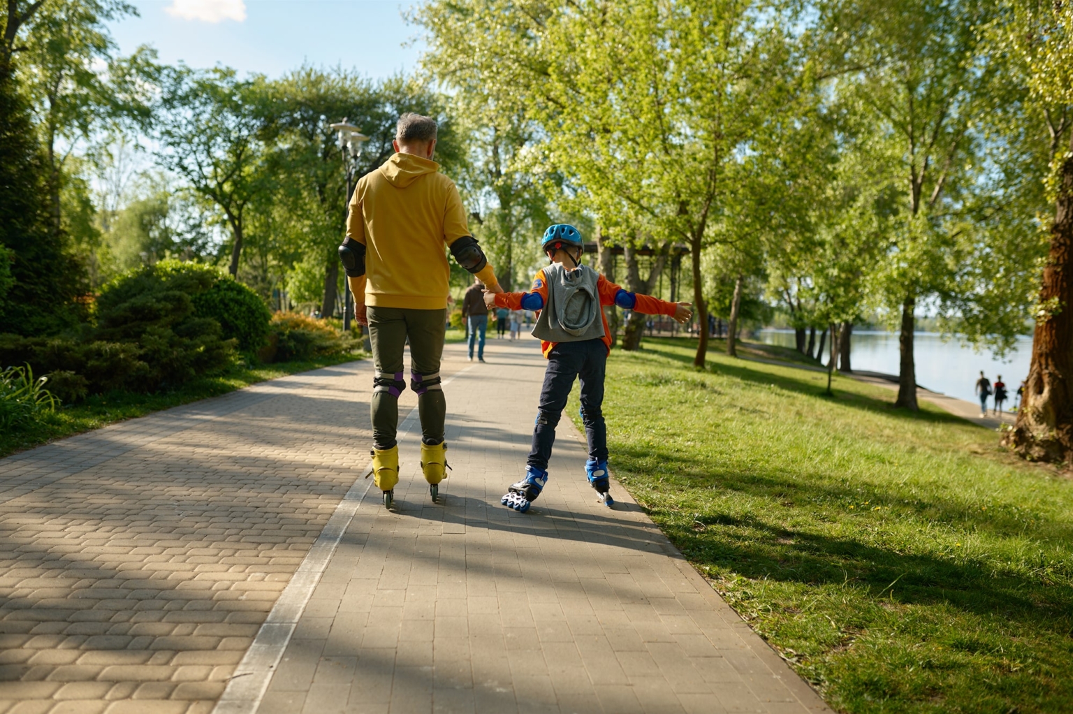 Otec a syn na kolečkových bruslích v parku v létě